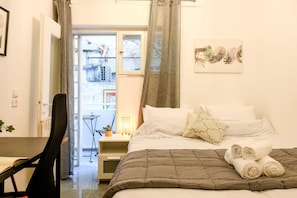 Quarto de hotel com uma cama, uma escrivaninha, uma cadeira, janela com cortinas e uma obra de arte pendurada na parede.