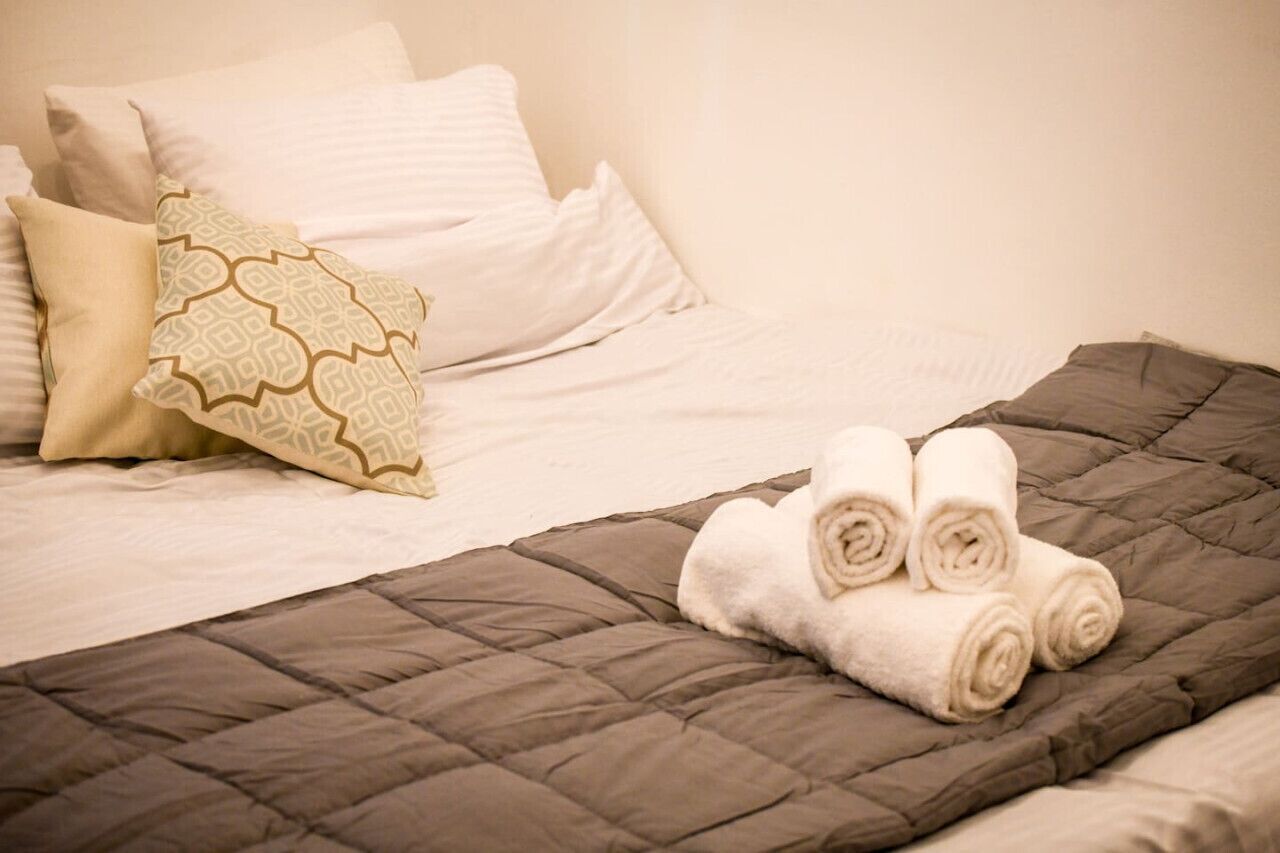 Una cama bien hecha con un edredón marrón oscuro, sábanas blancas y una almohada estampada.