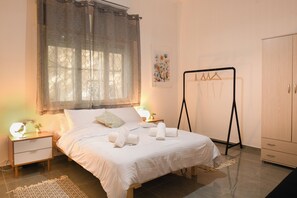 A neatly arranged bedroom with a bed, bedside tables, a wardrobe, and a window with curtains. - Charming 2BR in Haifa by Sea N' Rent (Haifa)