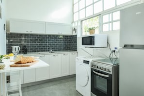 Cozinha moderna com armários brancos, painel de azulejos pretos, micro-ondas, máquina de lavar e forno.