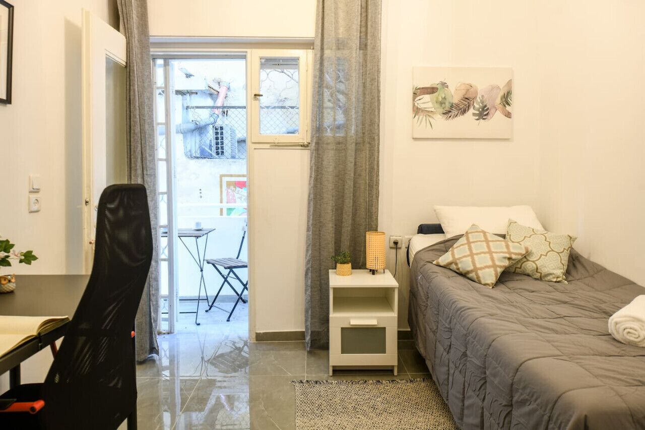 A bedroom with a bed, a chair, a small table with a lamp, and a window with curtains.