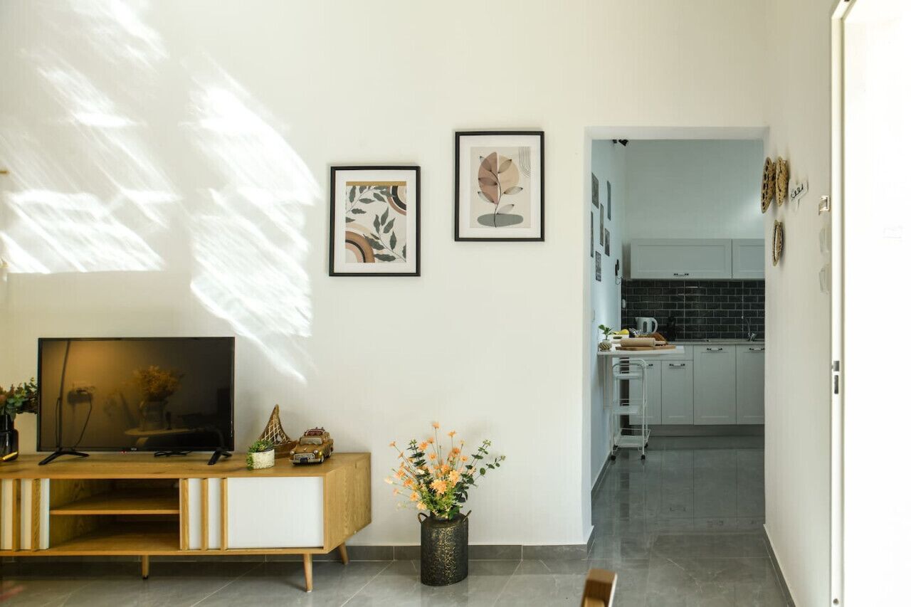 A modern living room with a TV, a wooden console, and a vase of flowers. There are two framed artworks on the wall.