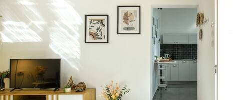 A modern living room with a TV, a wooden console, and a vase of flowers. There are two framed artworks on the wall.