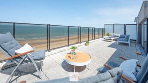 Una terrazza sul tetto con vista sulla spiaggia, arredata con sedie e un tavolo, e un cartello che indica 'Floor 1 Seaside'.