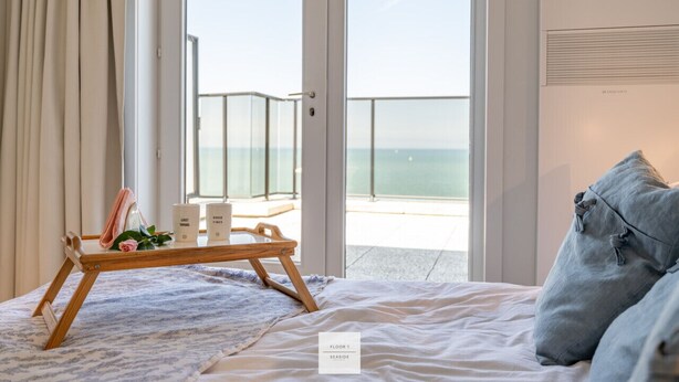 Camera da letto con un letto, un vassoio con degli oggetti e vista sul mare, e un cartello che indica "Floor 1 Seaside".
