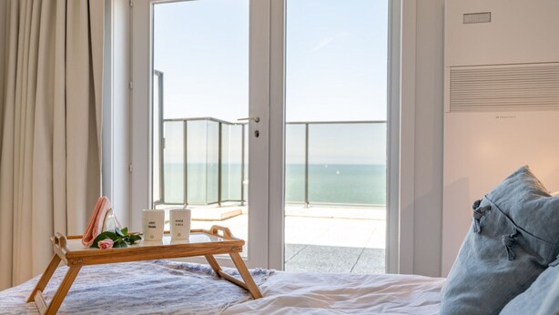 A bedroom with a bed, a tray with items, a view of the sea, and a sign indicating "Floor 1 Seaside".