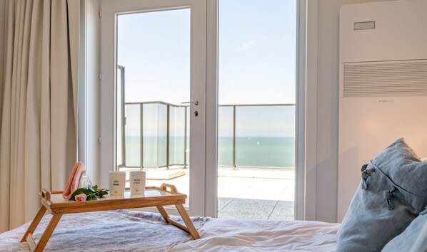 Un dormitorio con cama, un atril con objetos, vistas al mar y un cartel que indica 'Planta 1 Frente al Mar'.