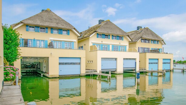 A row of thatched-roof houses with blue shutters, connected by a dock, reflecting in calm water. - perfect property for watersports enthusiasts (Stavoren)