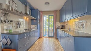 A kitchen with blue cabinets, wooden flooring, and a window with curtains. - perfect property for watersports enthusiasts (Stavoren)