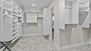 Un dressing accessible sans porte, doté de nombreuses étagères, de tiroirs et d’un espace pour suspendre les vêtements, avec une palette de couleurs neutres et un sol recouvert de moquette.