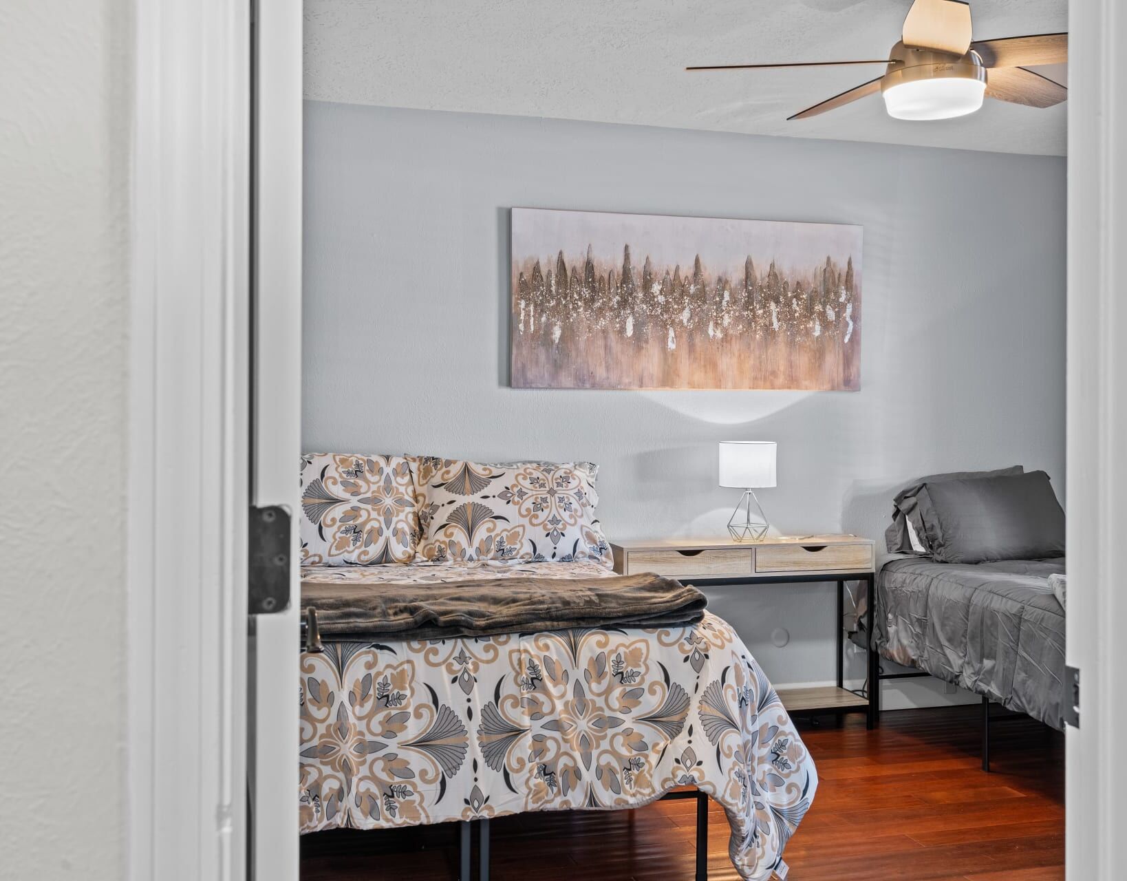 A bedroom with a bed, a bedside table with a lamp, a sofa, and a painting on the wall.