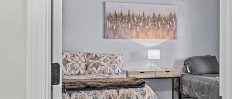 A bedroom with a bed, a bedside table with a lamp, a sofa, and a painting on the wall.