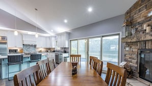 Una cocina moderna con armarios blancos, un comedor con mesa y sillas de madera, y una chimenea de piedra.