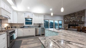Una cocina moderna con armarios blancos, encimera de granito y chimenea de piedra.
