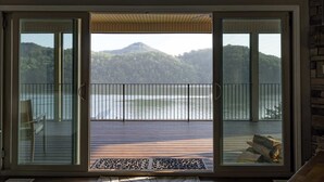 Una habitación con un amplio ventanal corredero que da a un balcón con vistas a un lago y colinas.