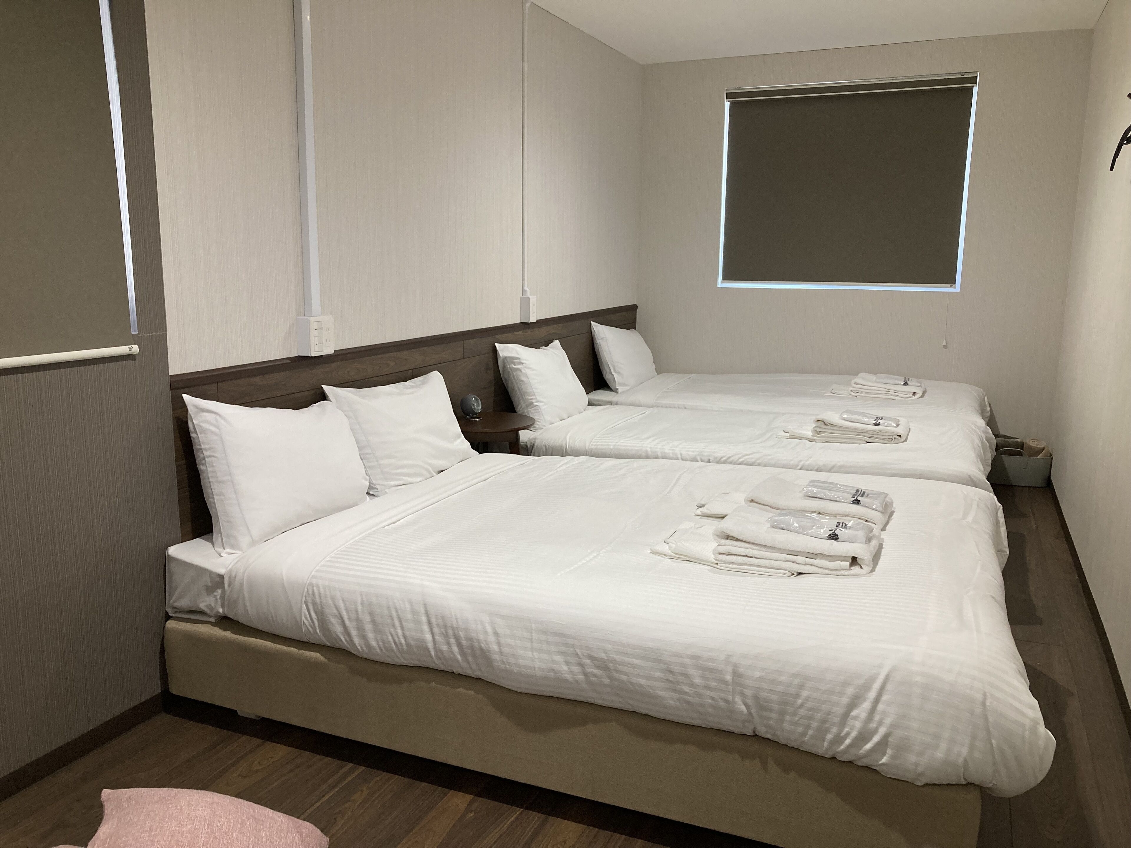 A hotel room with two beds, each with white linens and towels, a wooden headboard, and a small table with a lamp.