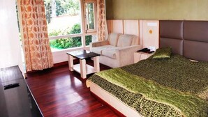 A bedroom with a bed, a small table, a sofa, and a window with curtains. - Hotel Green Top (Udhampur)
