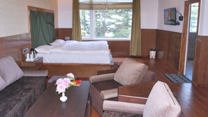 A hotel room with a bed, two sofas, a wooden table with a vase of flowers, and a window with curtains. - Hotel Green Top (Udhampur)