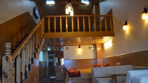 A spacious living area with a high ceiling, a wooden staircase, and a cozy seating area with a sofa and armchairs. - Hotel Green Top (Udhampur)