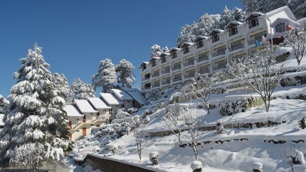 A snow-covered hotel with multiple floors, surrounded by trees and a clear blue sky. - Hotel Green Top (Udhampur)