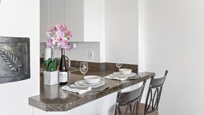 A kitchen with a granite countertop, white cabinets, and a dining area with two chairs and a table set for two. - 18th Fl Ilikai Hotel Condo | King Bed | Valet Parking | City View (Honolulu)