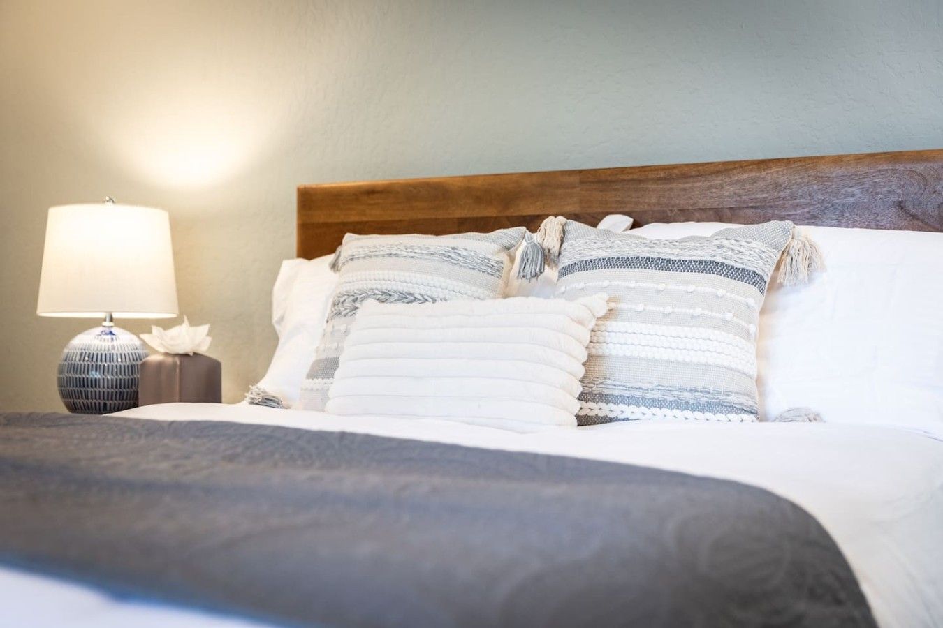 Un lit bien fait, avec une tête de lit en bois, une lampe de chevet et un coussin décoratif.