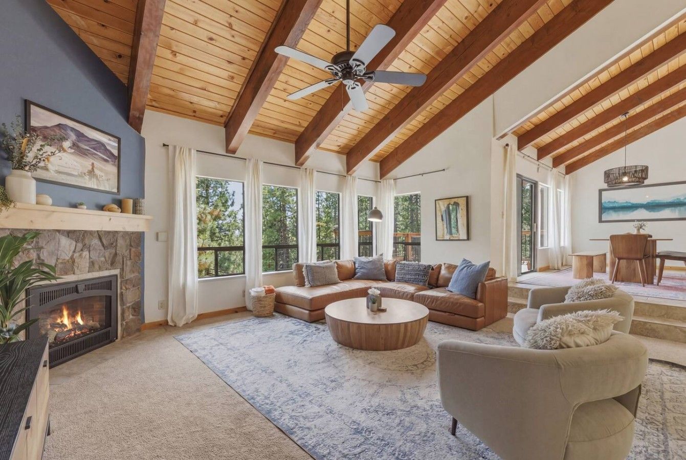 A spacious living room with a fireplace, a large sofa set, a round coffee table, and a ceiling fan.