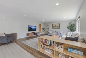 Un salon moderne avec un téléviseur à écran plat, une bibliothèque, un canapé gris et une table basse en bois.