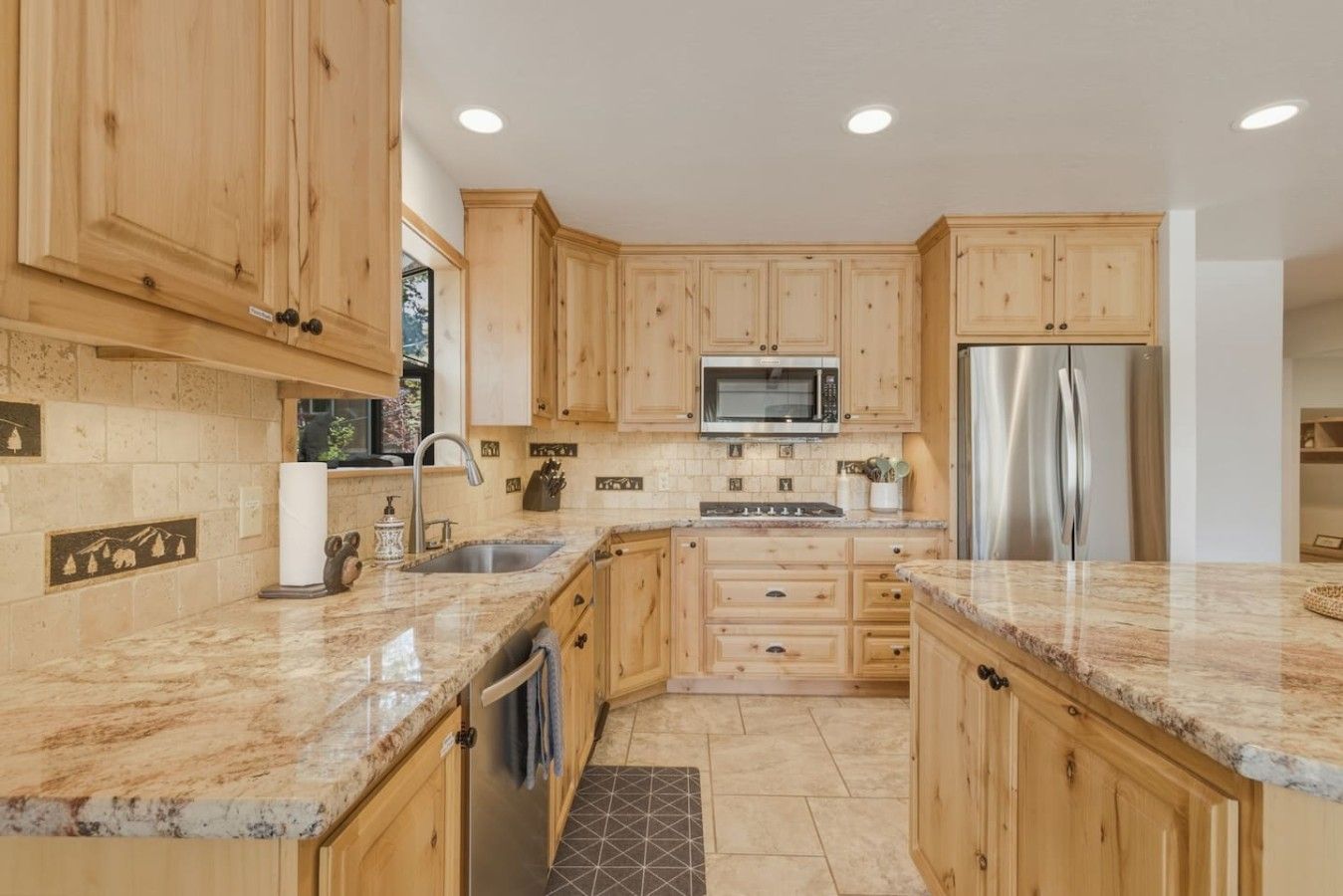 A kitchen with wooden cabinets, a stainless steel refrigerator, a microwave, and granite countertops.