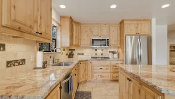 A kitchen with wooden cabinets, a stainless steel refrigerator, a microwave, and granite countertops.