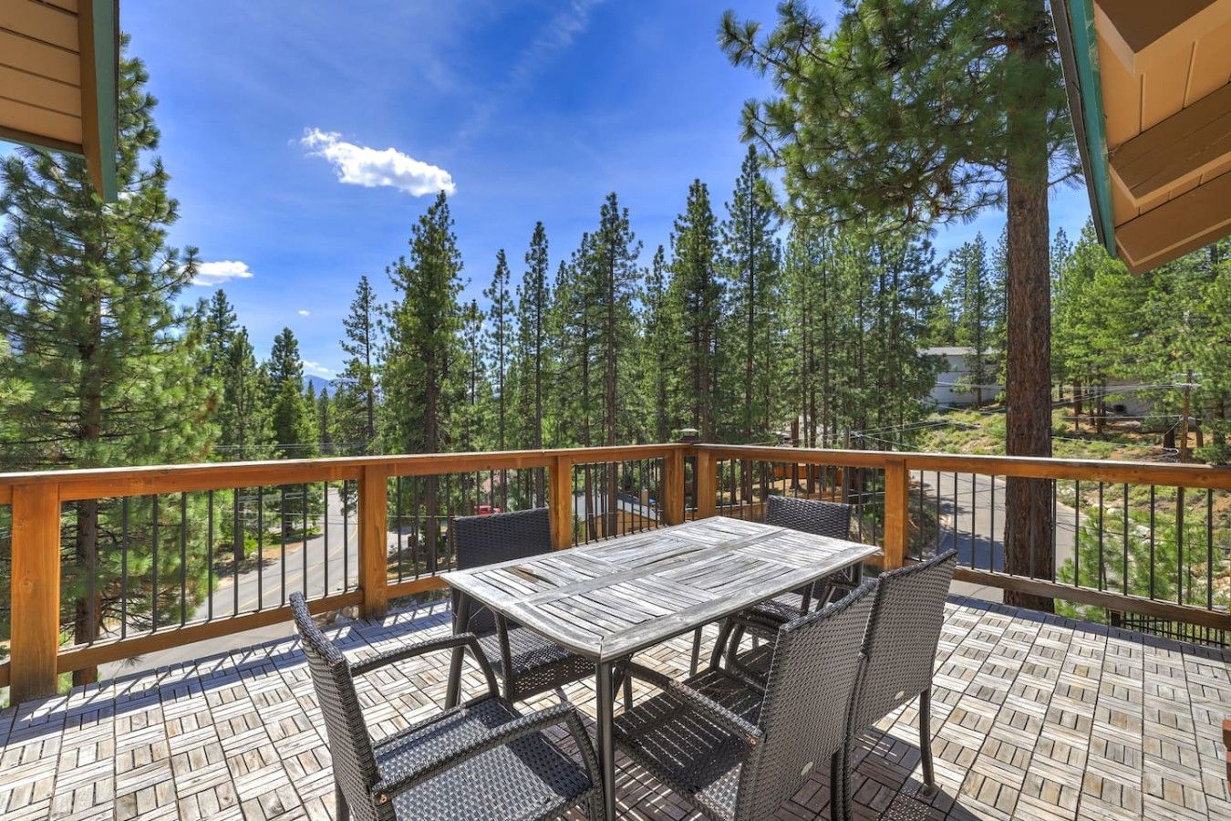 A deck with a table and chairs, surrounded by a wooden railing, overlooking a forested area.