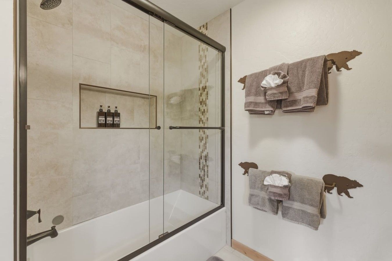 Een badkamer met een douchecabine van glas, een handdoekhouder met meerdere handdoeken en een plank met toiletartikelen.