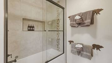 Een badkamer met een douchecabine van glas, een handdoekhouder met meerdere handdoeken en een plank met toiletartikelen.