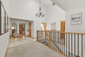 Un vaste hall d’entrée avec un escalier en bois, un lustre et des œuvres d’art encadrées accrochées aux murs.