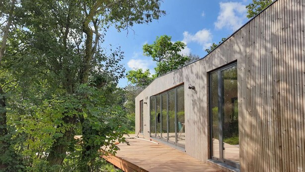 A modern wooden building with large windows, a wooden deck, and a natural surrounding. - Large modern holiday home with pool close to the beach (Groede)