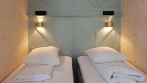 A room with two beds, each with a pillow and a folded towel, and a light-colored wooden headboard with a geometric pattern. - Large modern holiday home with pool close to the beach (Groede)