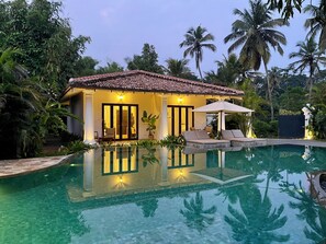 Una villa junto a la piscina con techo de tejas, una alberca y un área de descanso con toldo.