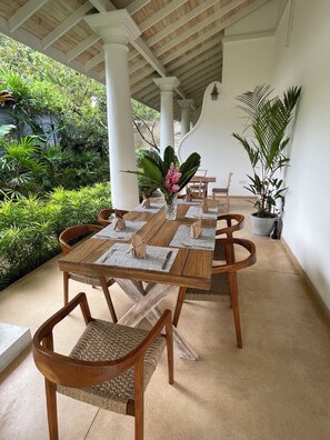 Un área de comedor al aire libre techada con una mesa de madera dispuesta para cuatro personas, rodeada de sillas de mimbre.