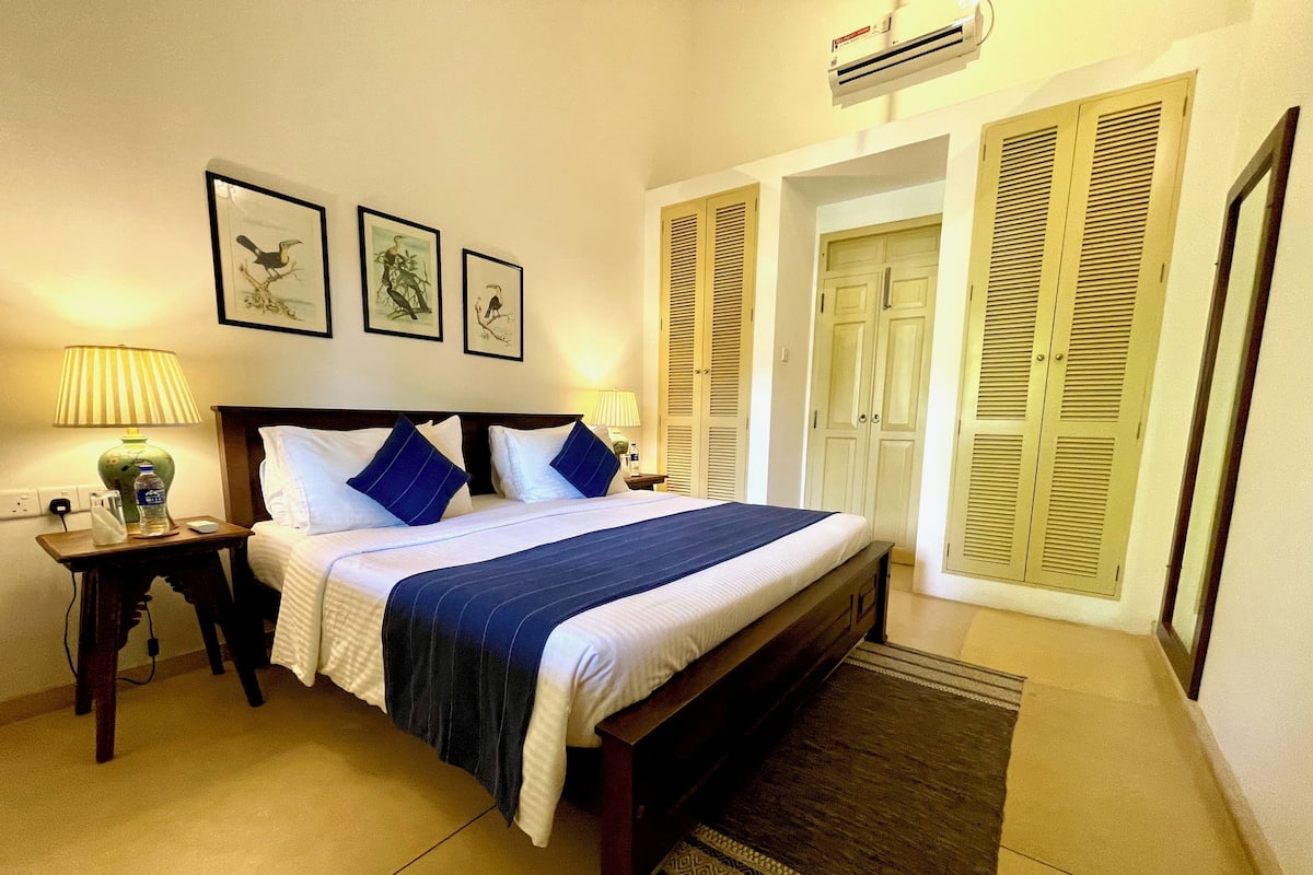 A neatly made bed with a blue and white bedspread, two bedside lamps, and three framed pictures on the wall.