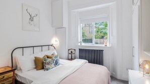 A bedroom with a bed, bedside table, radiator, window, and a framed picture on the wall. - The Barnsbury, London Apartment w/WIFI (London)