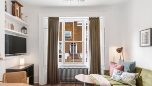 A modern living room with a green sofa, a wooden table, and a TV on a shelf. - The Barnsbury, London Apartment w/WIFI (London)