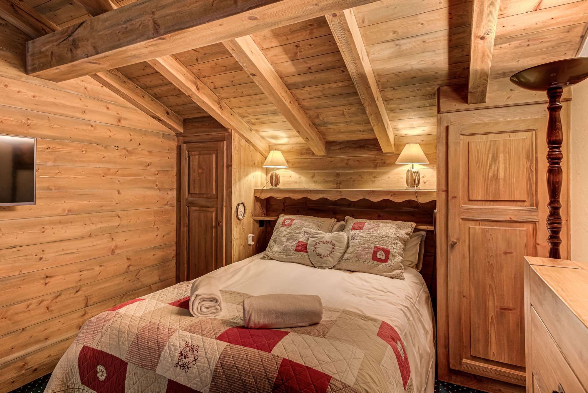 Een knus houten vertrek met een bed, twee bedlampen, een televisie en een kledingkast.