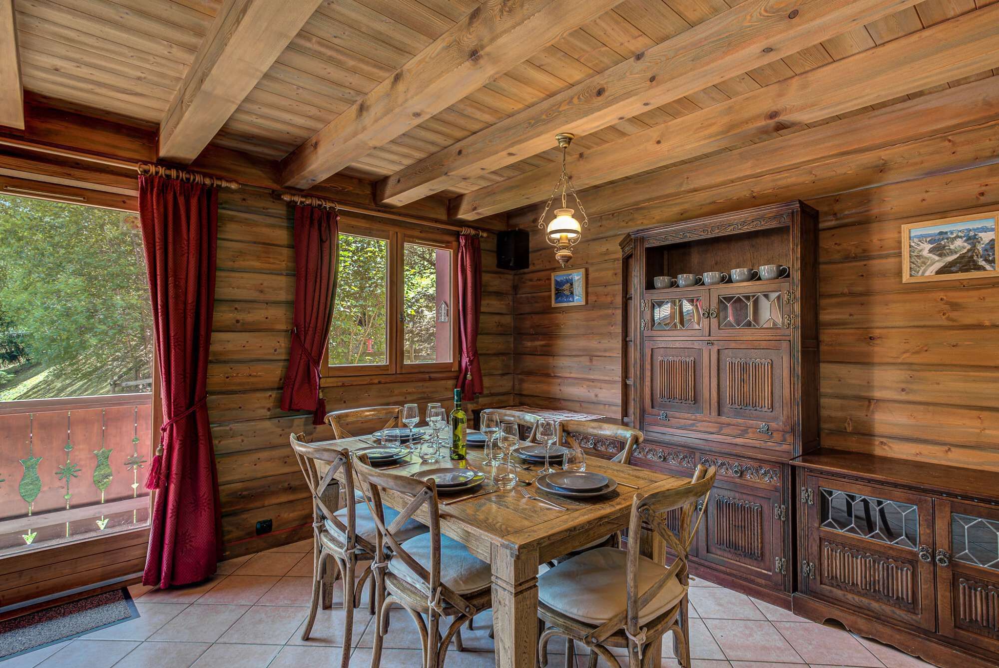 Een houten chalet eetruimte met een tafel voor vier personen, houten stoelen, een hanglamp en een kast met glazen deuren.