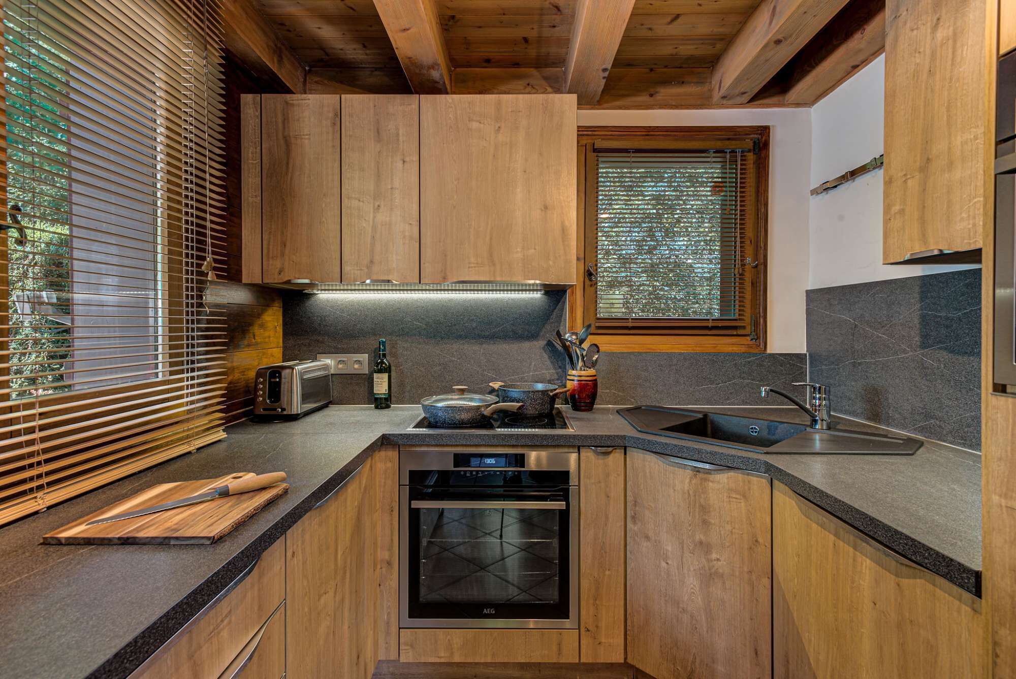 A modern kitchen with wooden cabinets, a built-in oven, a stainless steel sink, and a window with blinds.