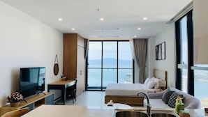 Une chambre d’hôtel moderne équipée d’un lit, d’un bureau, d’une télévision et d’une grande fenêtre donnant sur la mer.
