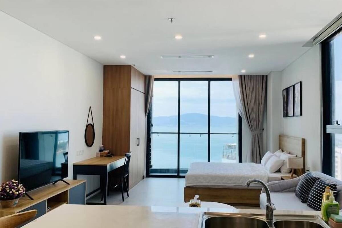 Une chambre d’hôtel moderne équipée d’un lit, d’un bureau, d’une télévision et d’une grande fenêtre donnant sur la mer.