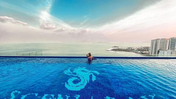 Une personne dans une piscine, avec vue sur l’océan et des bâtiments en arrière-plan.