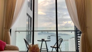 Een balkon met glazen hekwerk, een kleine ronde tafel, twee stoelen en uitzicht op een stadslandschap en water.