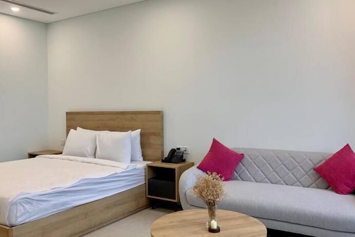 Une chambre d’hôtel moderne, équipée d’un lit, d’un canapé, d’une table de chevet avec un téléphone et d’un vase contenant des fleurs séchées.