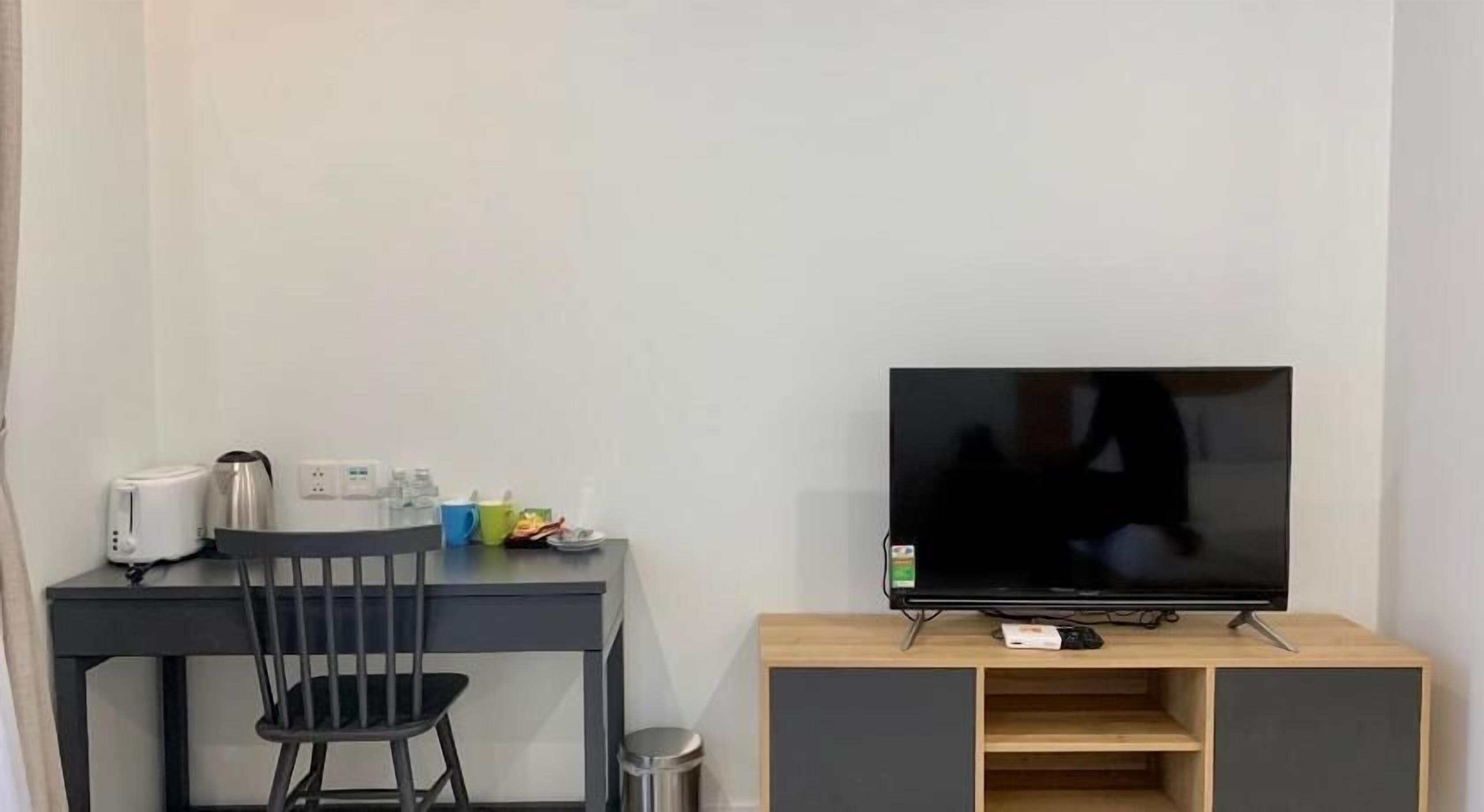 Een kleine, moderne kamer met een bureau, stoel en een televisie op een houten standaard.